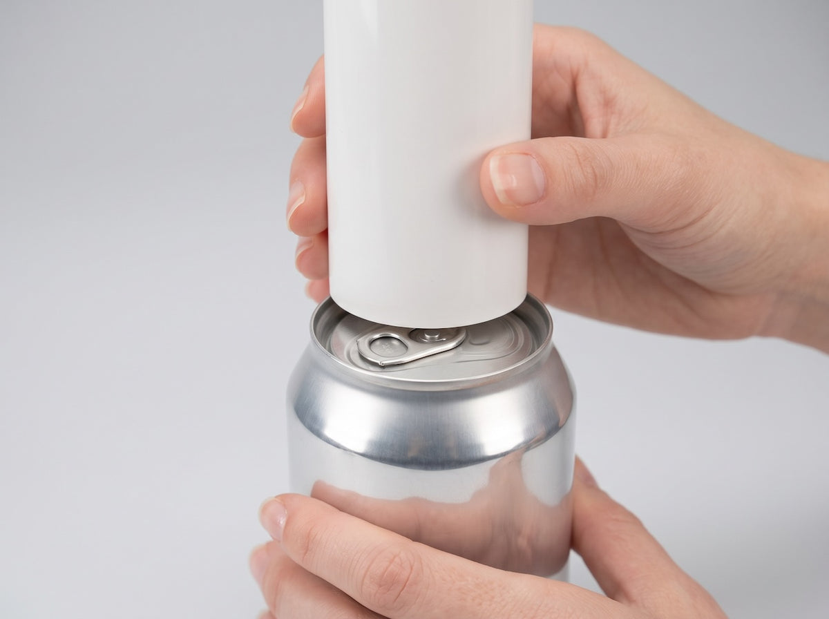 Hand holding a glossy white PVC pipe resting inside the rim on top of a soda can, showing the size of 1-1/2 inch PVC pipe.